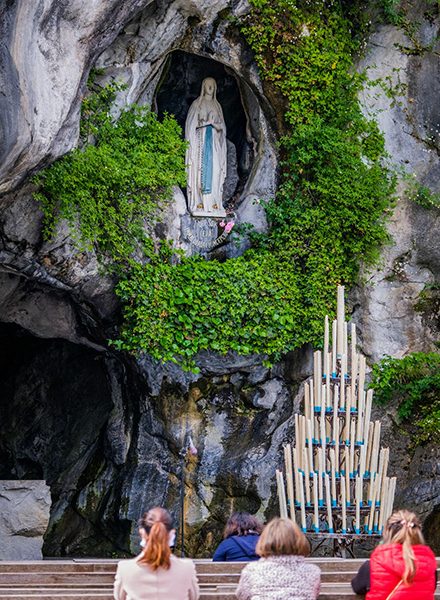 Peregrinos rezando em frente à gruta de Lourdes com a estátua de Bernadette Soubirous